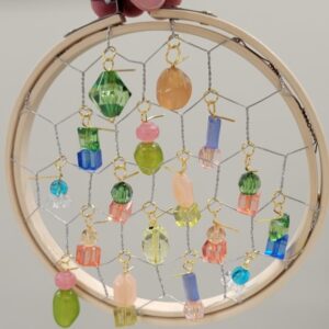 A wooden hoop with colorful beads hanging from a wire mesh.