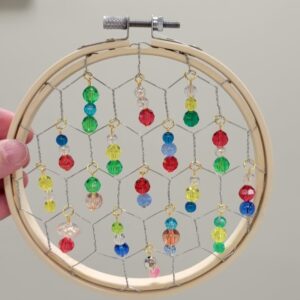 A circular wooden hoop with colorful beads hanging from a wire grid inside