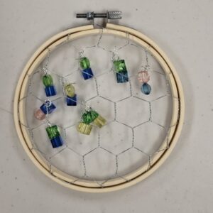 An embroidery hoop with wire mesh and colorful bead ornaments hanging on it