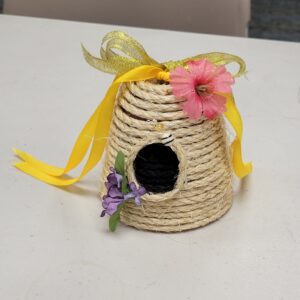 A small decorative beehive made of coiled rope with ribbon and flowers