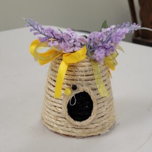 A decorative beehive with purple flowers and yellow ribbons on top.