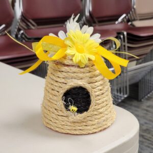 A rope beehive ornament with yellow flowers and a bow on a table