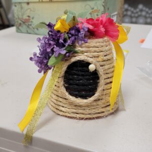 Decorative rope beehive with colorful faux flowers and yellow ribbon.