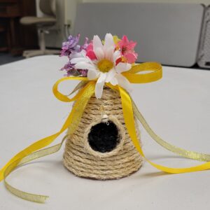 A decorative woven beehive with artificial flowers and a yellow ribbon.