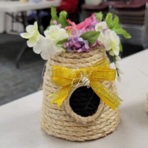 Miniature rope beehive with flowers and a gold bow.