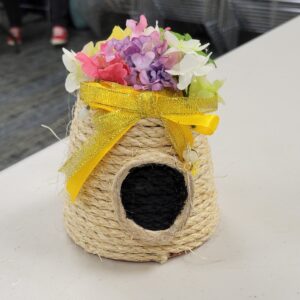 A decorative woven beehive with artificial flowers and a yellow ribbon