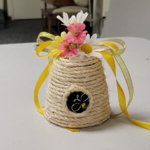 A decorative beehive made of twine with flowers and a ribbon on top